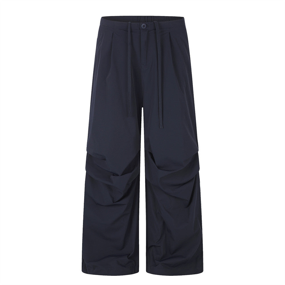Men's navy wide-leg parachute pants with front pleats, ruched lower-leg panels, and drawstring waistband, shown from front an