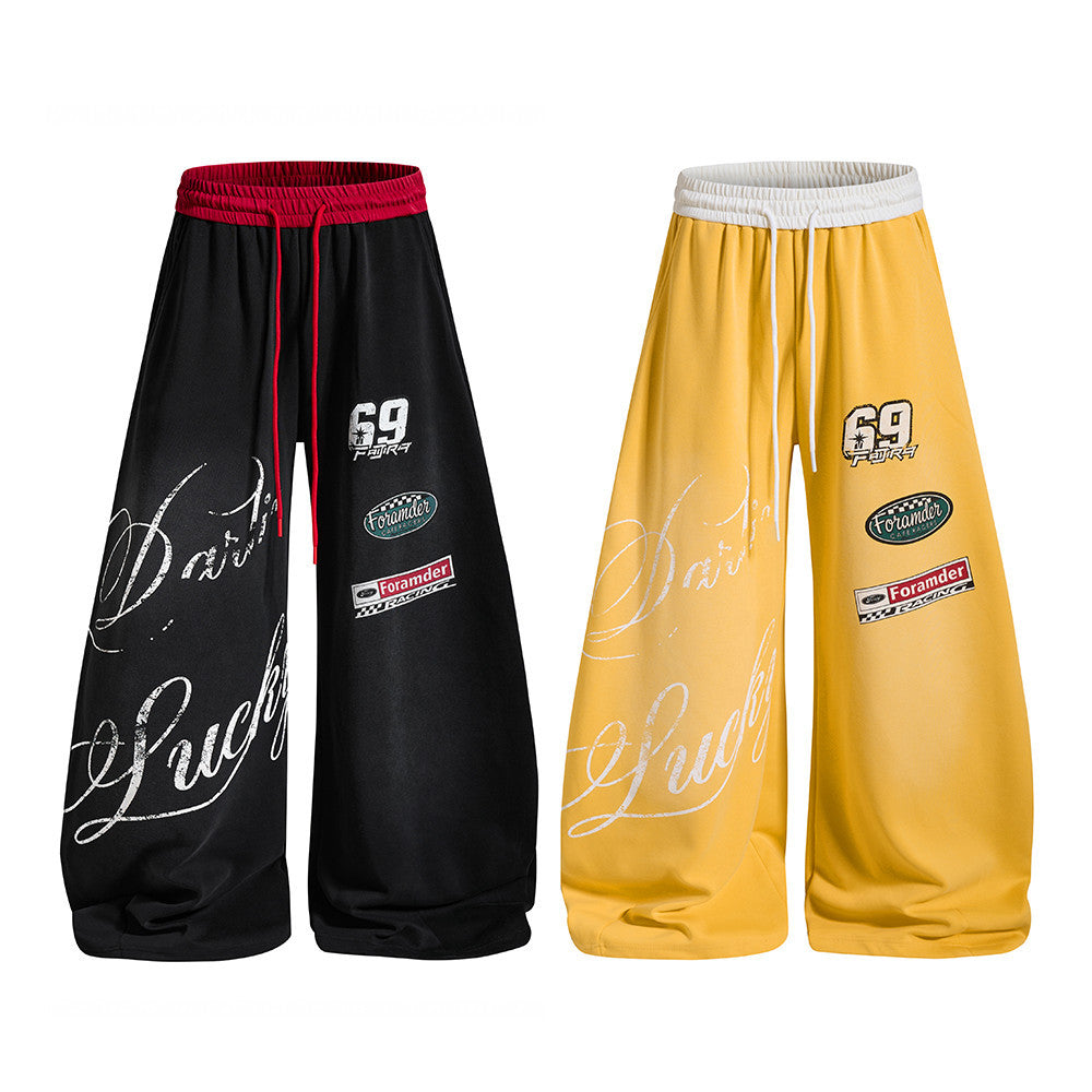 Wide-leg racing graphic sweatpants in black with red contrast waistband and cursive letter print, shown alongside yellow colo