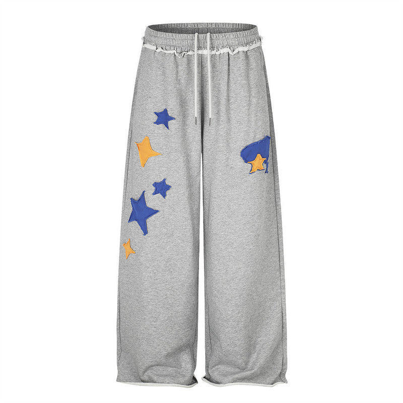 Pantalon de survêtement homme gris chiné à jambes larges, avec appliqués étoiles bleus et orange et ceinture à cordon effilochée