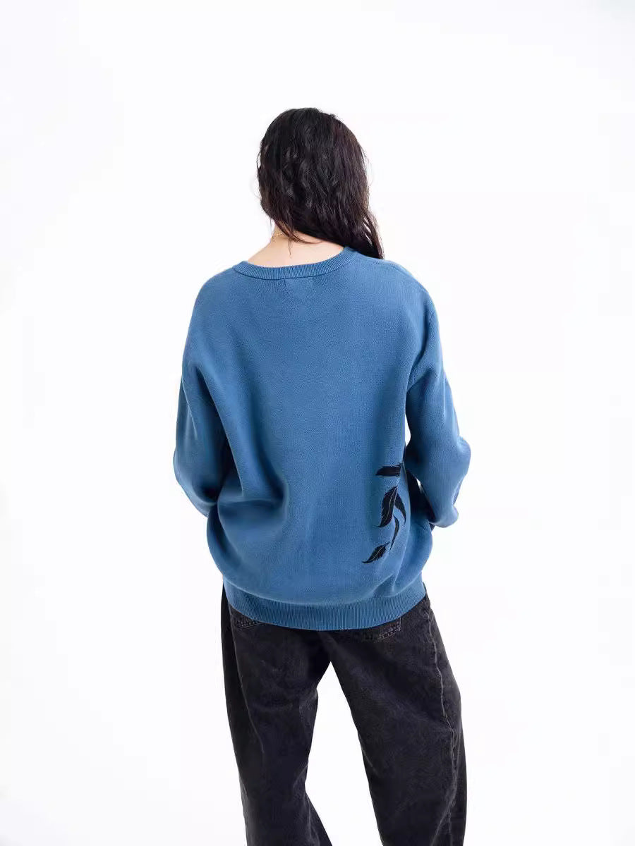 A person, with long dark hair and hands in pockets, faces away wearing Seakoff's Premium Howl’s Moving Castle-Inspired Knit Sweater featuring a Howl & Sophie starry jacquard design and black pants. The background is plain white.