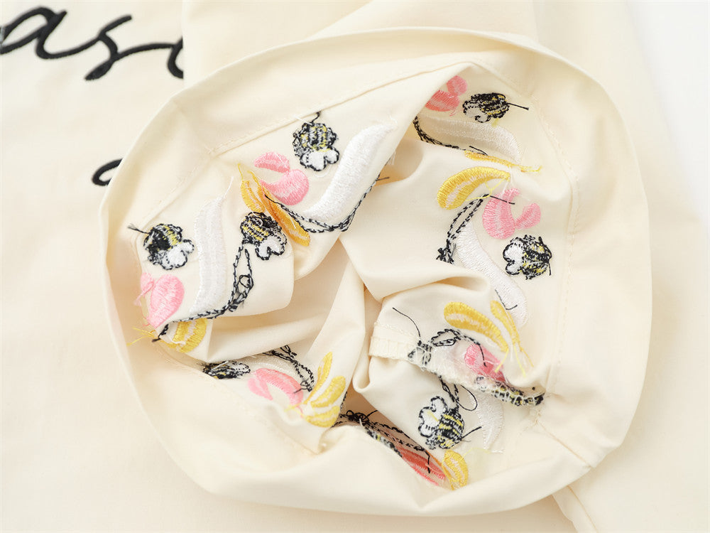 Close-up of cream shirt cuff showing multicolor floral and bee embroidery