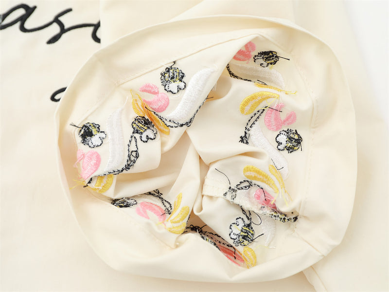 Close-up of cream shirt cuff showing multicolor floral and bee embroidery