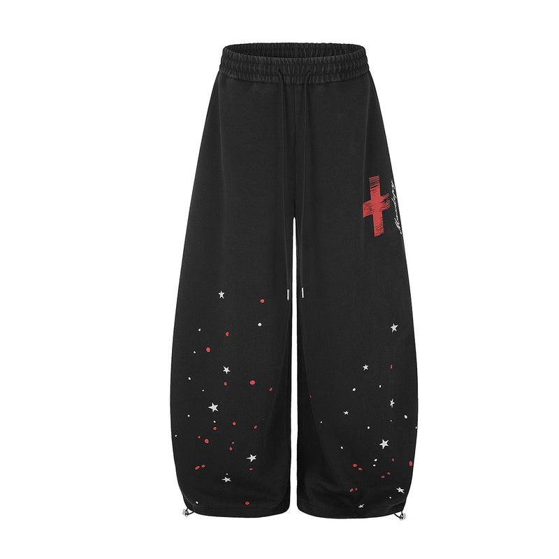 赤いクロスと白い星の散りばめプリントを施したブラックのワイドレッグスウェットパンツ。前後ビュー