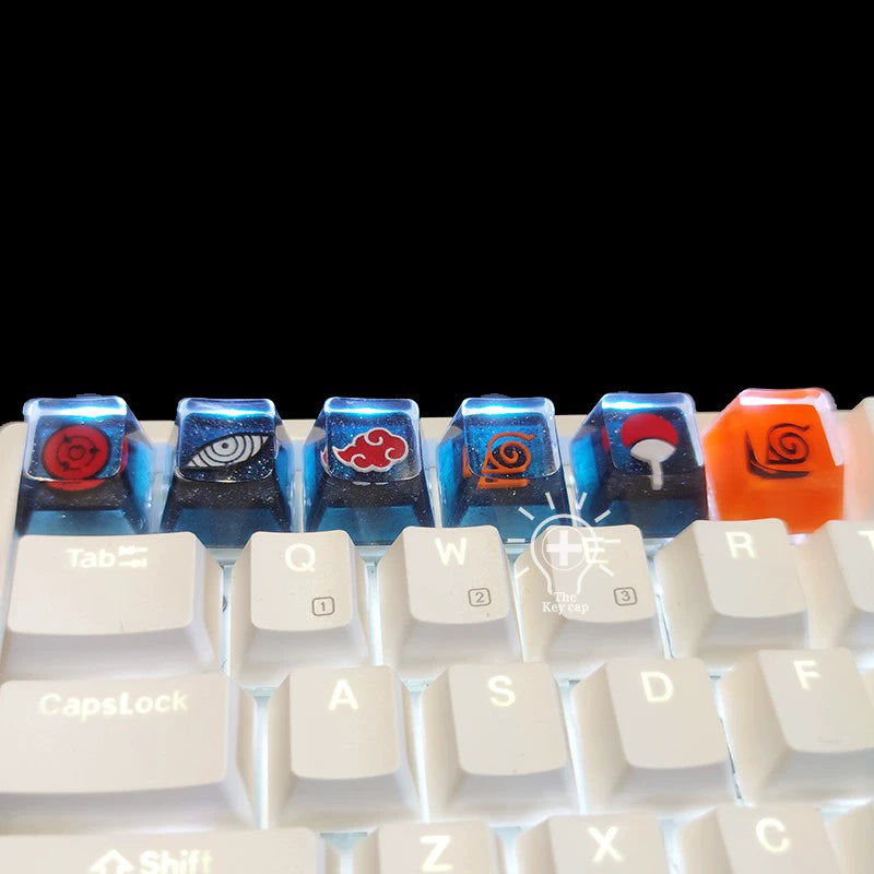 The Naruto Symbols Keycap Set from the Naruto brand includes six customized designs, featuring Hidden Village, Uchiha, and Akatsuki symbols in vibrant colors on a white keyboard. Made of high-quality resin, these keycaps for the number row above QWERTY have an enchanting illuminated effect.