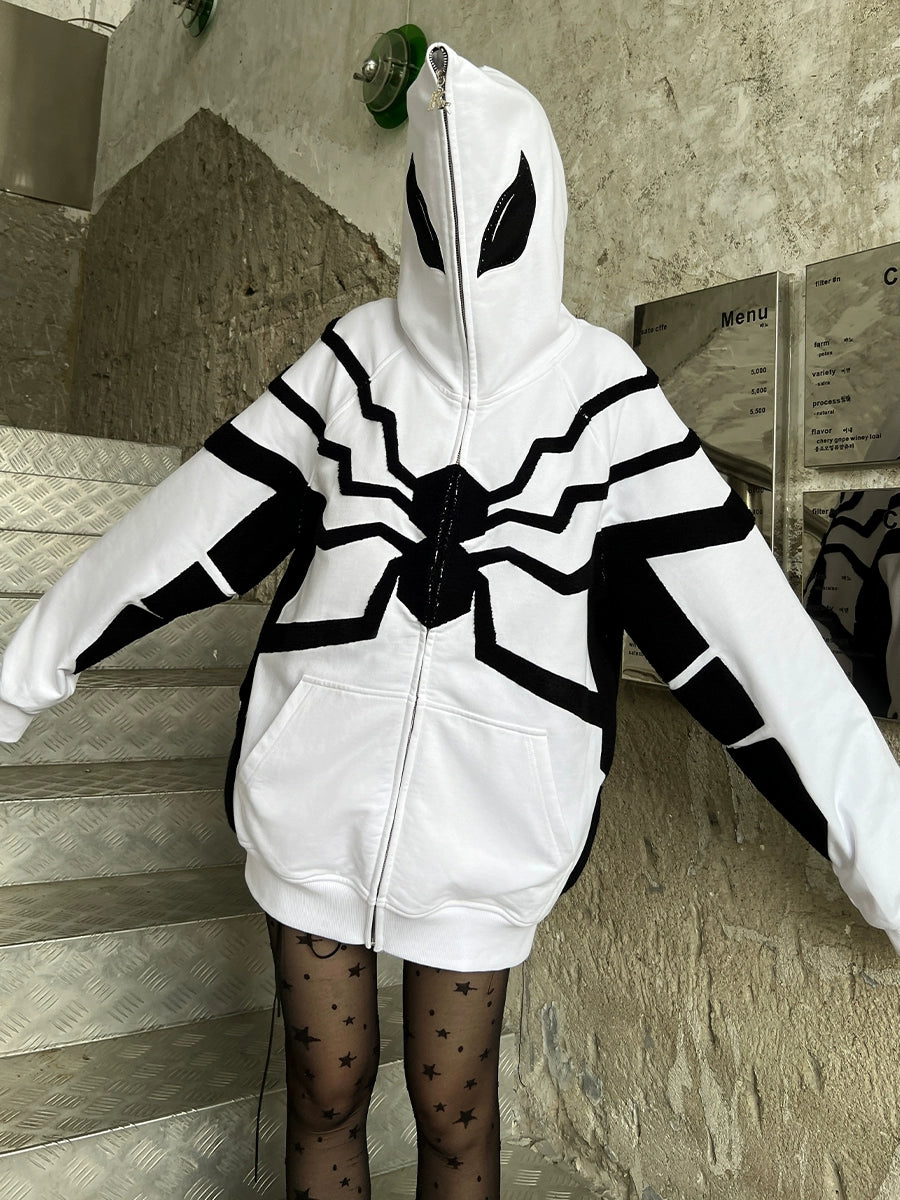 A person, hood up, stands on stairs in a Seakoff Venom-Inspired White Hoodie - an oversized Spider zip-up superhero sweatshirt made from 400GSM cotton. The hoodie boasts a large black spider design on white fabric with deep black accents, paired with sheer star-patterned black tights.