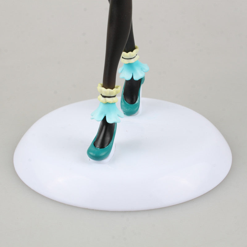 A close-up showcases the legs of the Hatsune Miku 1/7 Scale PVC Figure in teal high heels with light blue ruffles, positioned on a white circular base against a neutral gray background, highlighting a darker skin tone.