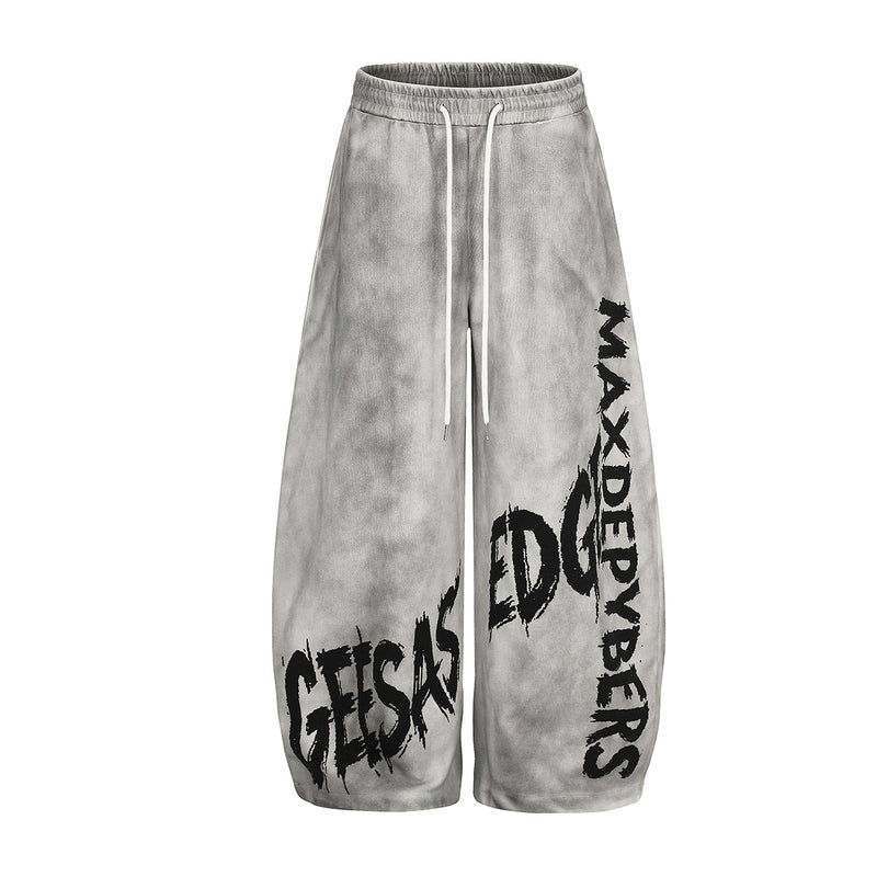 Oversized wide-leg acid-wash sweatpants with bold graffiti text print on both legs in light grey