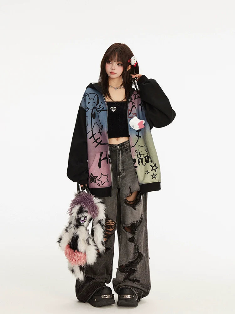 A person stands against a plain background wearing the Seakoff Pastel Cat Graffiti Hoodie – a full-zip hoodie with colorful cat and star graphics, paired with a black crop top and ripped jeans. They're holding a unique furry bag, have headphones on, and their sleek dark brown hair enhances the streetwear vibe.