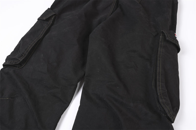 Close-up of black cargo pant thighs with side flap pockets and studded trim