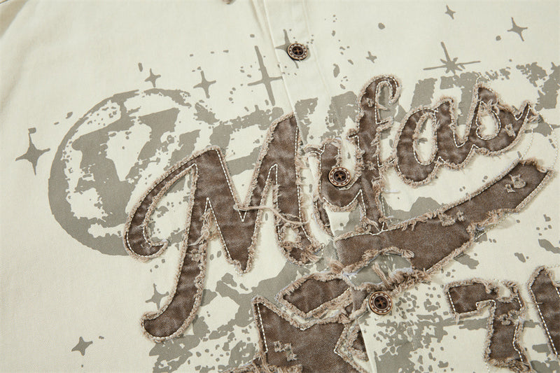 Close-up of chest graphic on cream shirt with distressed brown lettering and buttons