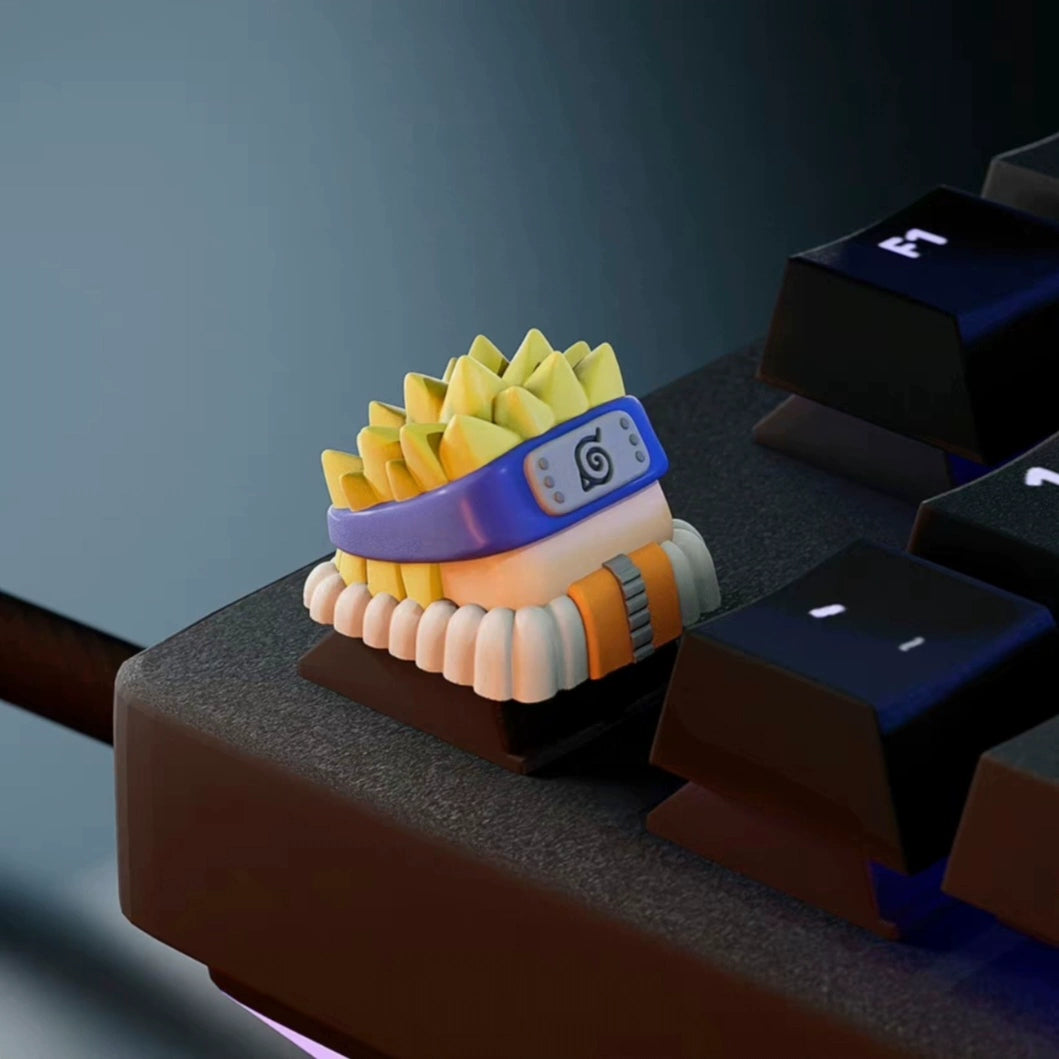 A small, premium Naruto keycap from the Naruto Keycaps Set features an anime character with spiky yellow hair, a blue headband, and an orange collar. Ideal for fans, it enhances a dark keyboard under soft lighting.