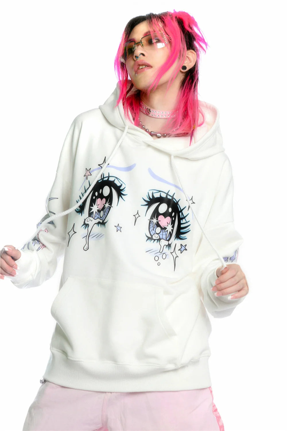 A person with pink hair flaunts Seakoff's Kawaii Aesthetic Crying Eyes Hoodie, a white anime-style pullover with sleeve graphics. They wear pink-tinted sunglasses and a choker necklace, blending streetwear fashion with playful charm against a plain white backdrop, highlighting their unique style.