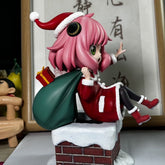 The Anya Forger Christmas Outfit Figure from Spy × Family features a charming figure on a chimney, wearing a Santa outfit with pink hair. Accompanied by a green sack and gift box, it includes Chinese character details and a wooden toy stand, making it ideal for anime collectors.