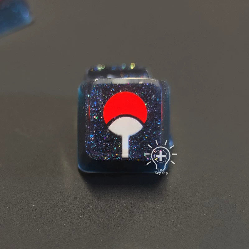 The Naruto Symbols Keycap Set features a premium black resin keycap with a glittery surface, illuminating effect, and an eye-catching red and white fan symbol.