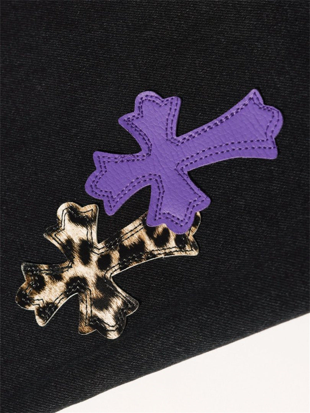 Close-up of purple and leopard cross patches on black denim, angled view