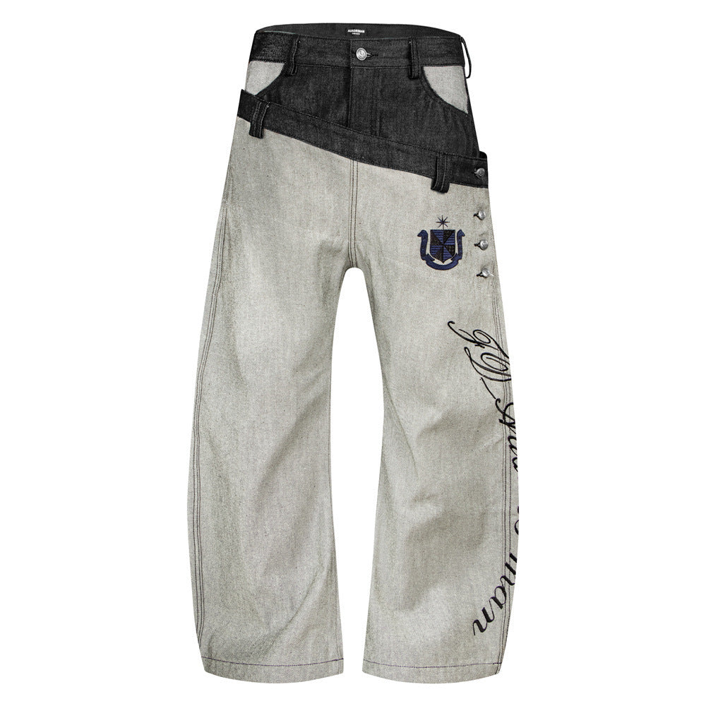 Jean ample en denim brut à double ceinture, empiècement diagonal contrasté, écusson brodé et inscription cursive sur la jambe —