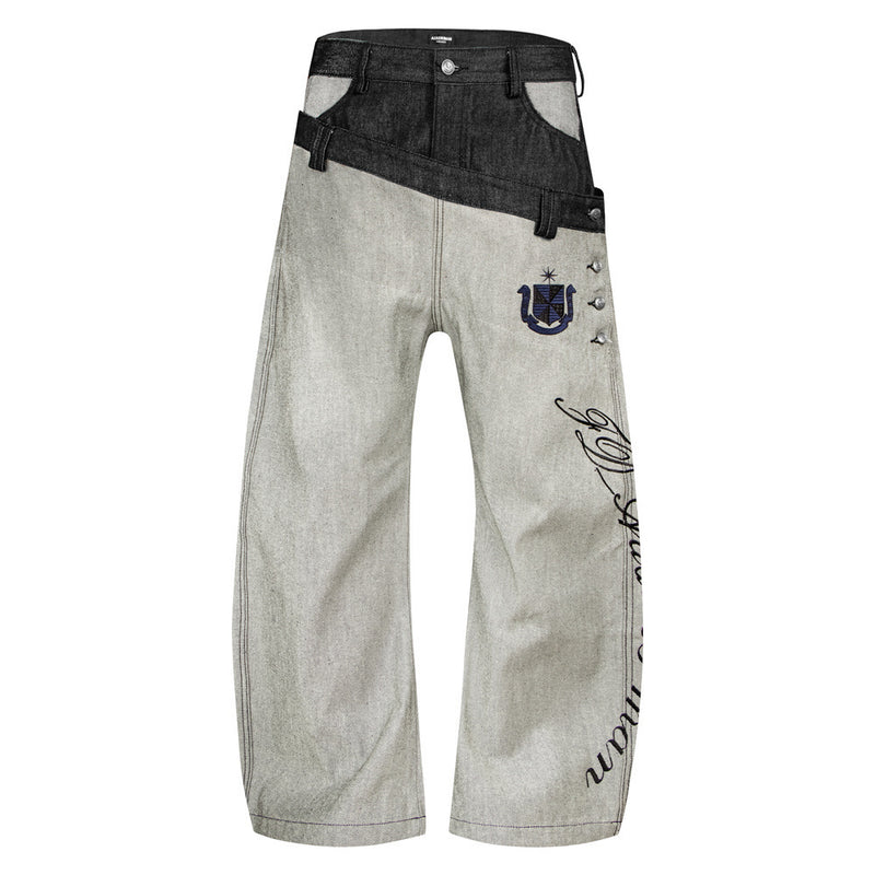 Jean ample en denim brut à double ceinture, empiècement diagonal contrasté, écusson brodé et inscription cursive sur la jambe —