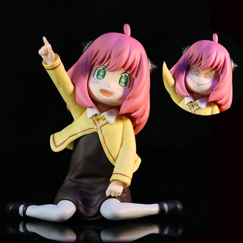 The Anya Forger in Yellow School Uniform - Interchangeable Face PVC Anime Figure from the Spy × Family brand showcases her with pink hair, large green eyes, and a playful pose in a yellow jacket and black dress. Another face option features her smiling with closed eyes, perfect for your collection.