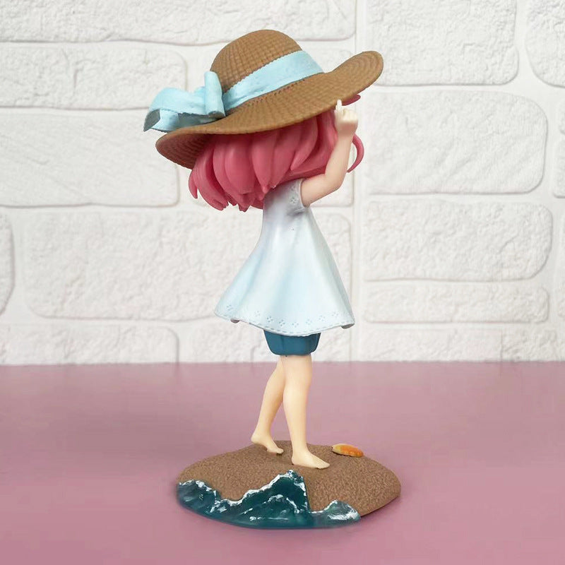 The Anya Forger Beach Day PVC Figure from the Spy × Family Summer Collection features a girl with pink hair in a light blue dress and blue shorts, wearing a wide-brimmed brown hat with a blue ribbon. She stands on a sandy base with water, backed by a textured wall. Height: 17cm.