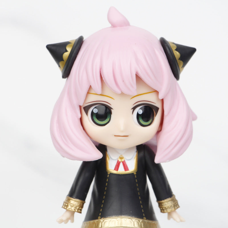 The Spy x Family Complete Set includes a 15cm chibi-style Anya figure with pink hair, large green eyes, and two black triangular head accessories. She wears a black outfit with gold details and a white collar, reminiscent of the character&