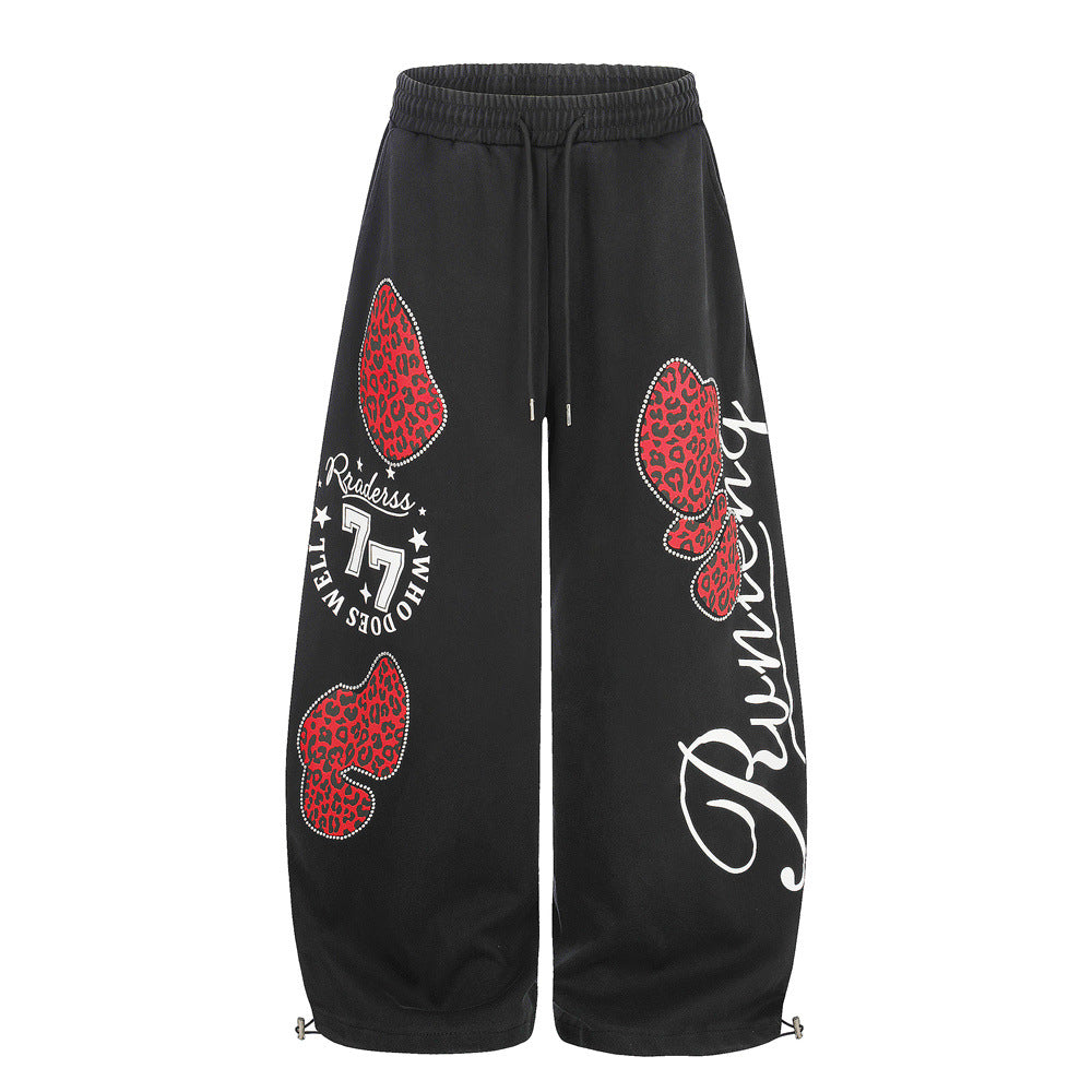 Wide-leg sweatpants in black with red leopard-print rhinestone heart graphics and cursive Running script on the leg