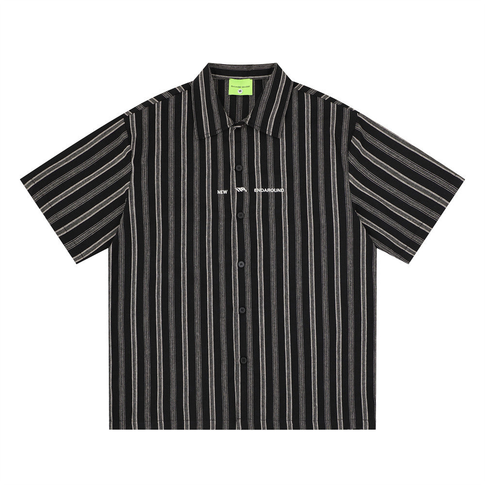 Oversized vertical stripe short sleeve button-up shirt in black with white stripes, front view showing spread collar and logo
