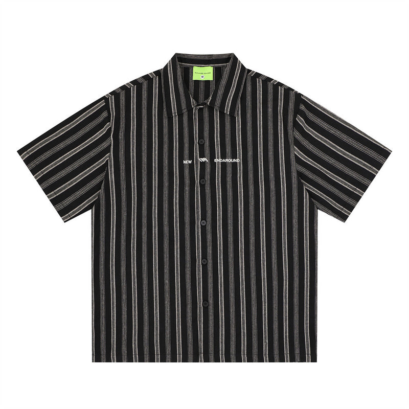 Oversized vertical stripe short sleeve button-up shirt in black with white stripes, front view showing spread collar and logo