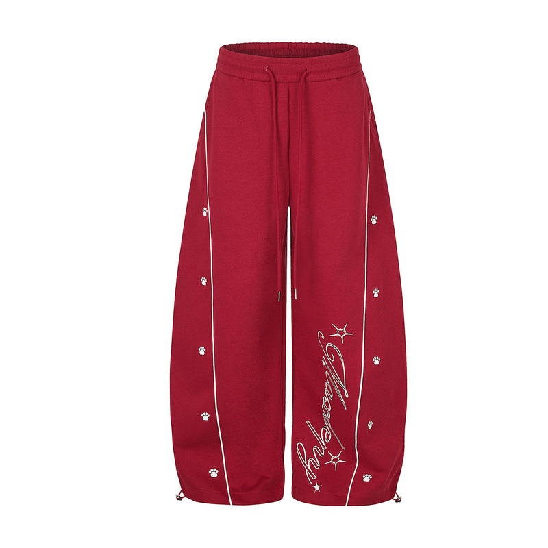 Pantalon de survêtement rouge à jambes larges avec passepoil blanc contrastant, motifs de pattes et détail de lettrage cursif au bas, vues de face et de dos