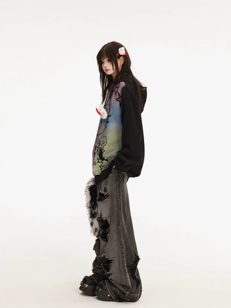A person stands in profile showcasing streetwear flair with Seakoff's Pastel Cat Graffiti Hoodie, full-zip and adorned with a colorful cat and star design. Their long dark gray distressed jeans and platform shoes complete the look. Long dark hair, held by a kawaii hairpin on the left, frames a plain white background.
