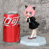 A 15cm PVC figure of a pink-haired, cat-eared character in black pajamas holds a teddy bear on a hexagonal base, similar to the Spy x Family Anya Forger Bear Pajamas Collectible. A red soda can with white writing stands beside it.