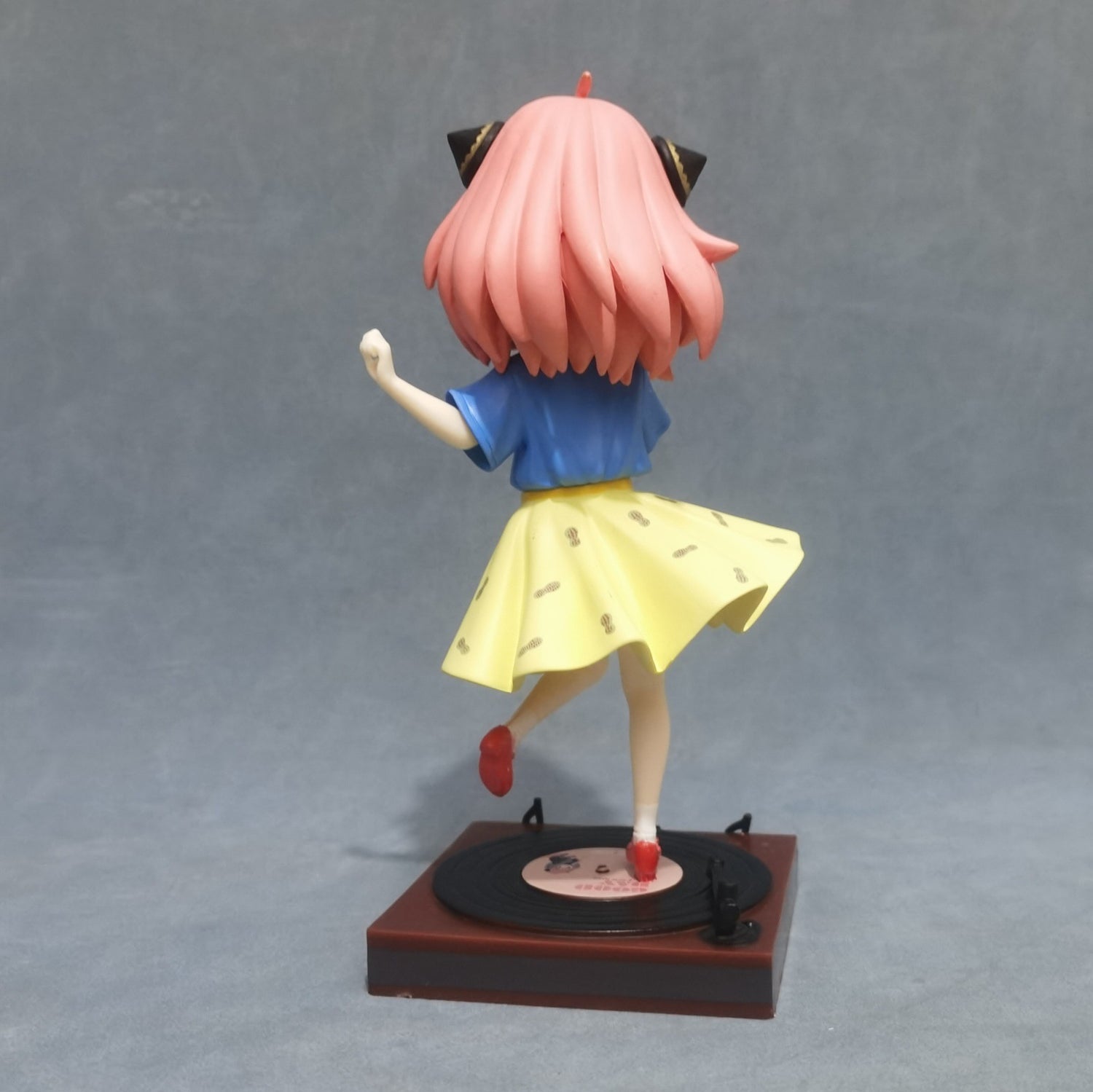 The limited edition Anya Forger Dancing Figure from Spy × Family features a pink-haired girl with cat ears in a blue shirt and yellow skirt, posed mid-step on a vinyl record stand. This whimsical 18cm PVC anime figure is perfect for any collection.