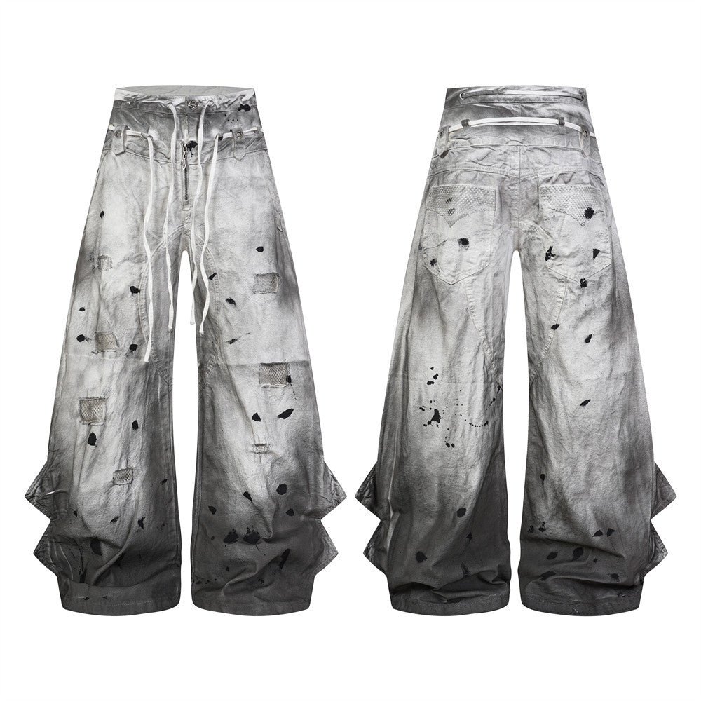 Distressed wide-leg jeans in dirty-wash gray gradient with ink splatter, mesh patches, exposed zipper, and double waistband l