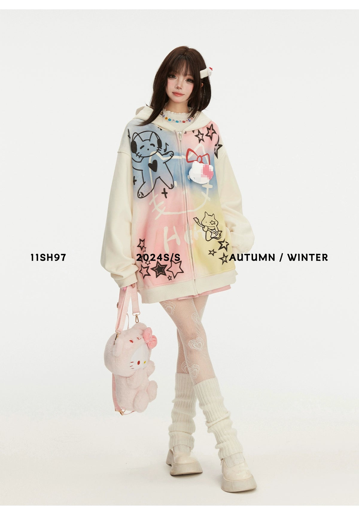 A model showcases the Seakoff Pastel Cat Graffiti Hoodie featuring colorful cat and star graphics for a streetwear vibe. She carries a matching kawaii plush bag, with knee-high socks and chunky shoes completing the look. Text reads &quot;11SH97&quot; and &quot;2024 S/S AUTUMN / WINTER.