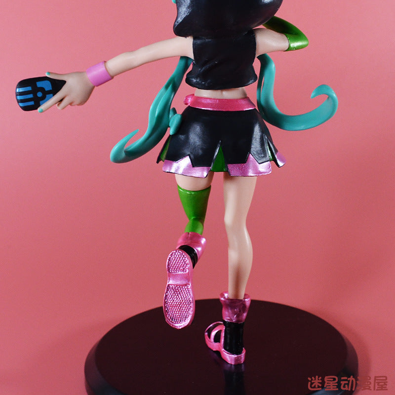 The Hatsune Miku Cat Hoodie 17cm PVC Figure features an anime-style character with teal hair, wearing a black and pink outfit with green accents and a cat hoodie, holding a gaming controller. She stands on a round black base against a pink background.