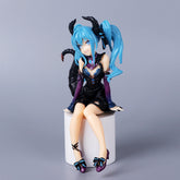 The Hatsune Miku Little Demon Sitting Pose 11cm PVC Figure features blue hair, black horns, and a striking black and blue outfit with purple accents. It elegantly perches on a white base with playful blue bow-adorned black shoes, making it a stylish & bold collectible.