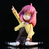 This adorable Anya Forger in Yellow School Uniform PVC figure from the Spy × Family series showcases a pink-haired character in a yellow jacket and brown skirt, seated with a smile and one arm raised against a black backdrop—an essential for anime collectibles enthusiasts.