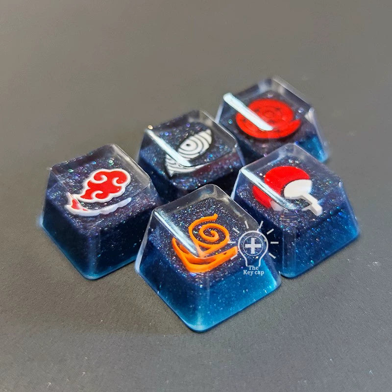 Five custom keycaps from the Naruto Symbols Keycap Set are beautifully displayed on a dark surface. Each keycap made by Naruto features high-quality resin with red, white, and orange symbols and logos on a sparkly blue background that creates an illuminated effect.