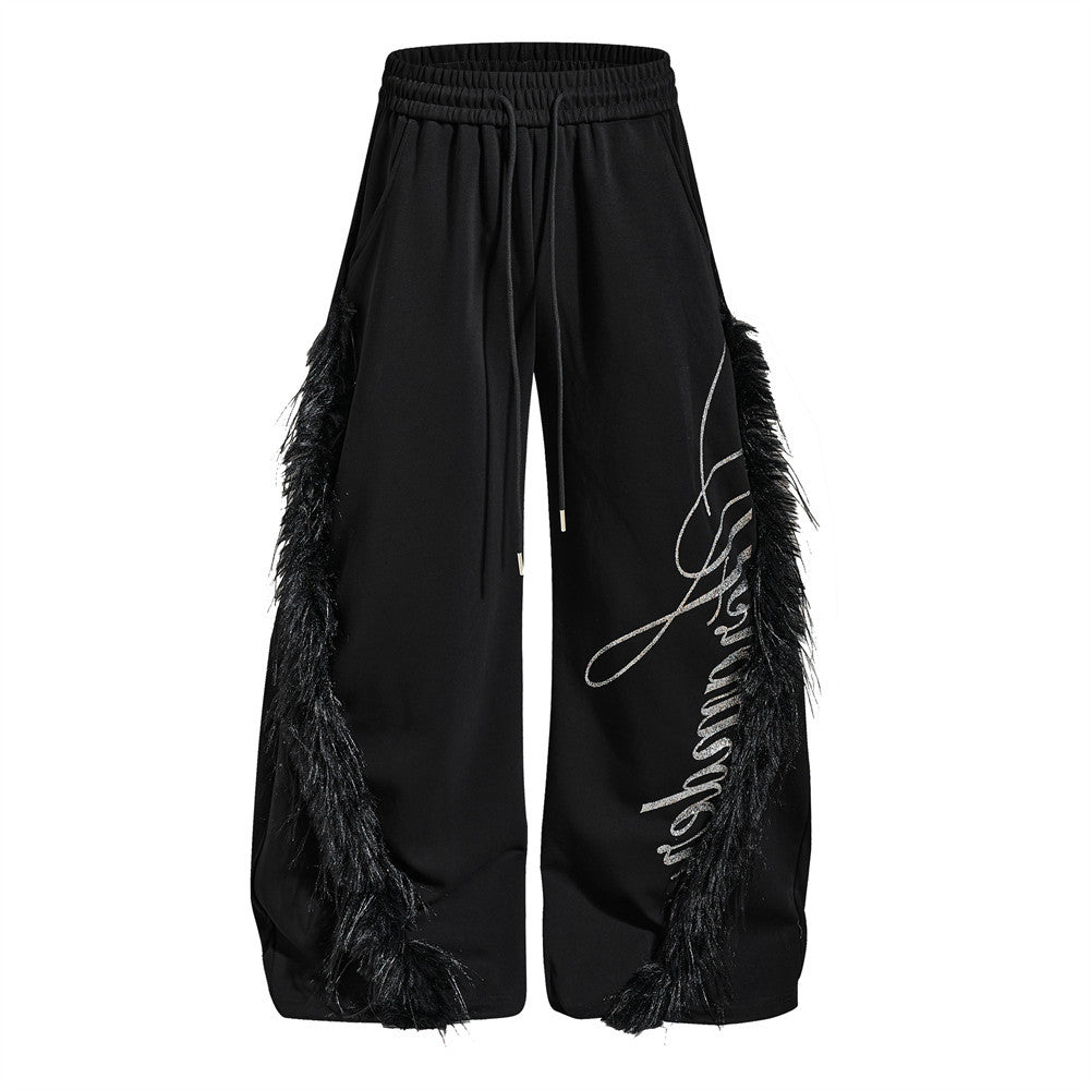 Black baggy wide-leg pants with feather side trim and rhinestone cursive script graphic on front leg