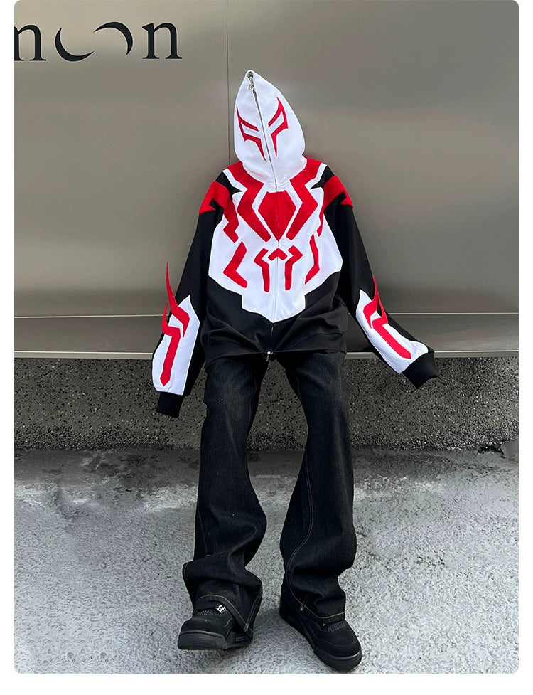 A figure sits against a wall, face obscured by a Seakoff Superhero-Inspired Hoodie, featuring black, red, and white patterns. The oversized 400GSM zip-up sweatshirt pairs with black pants and shoes—ideal for streetwear fans. Abstract text is partially visible on the wall behind.