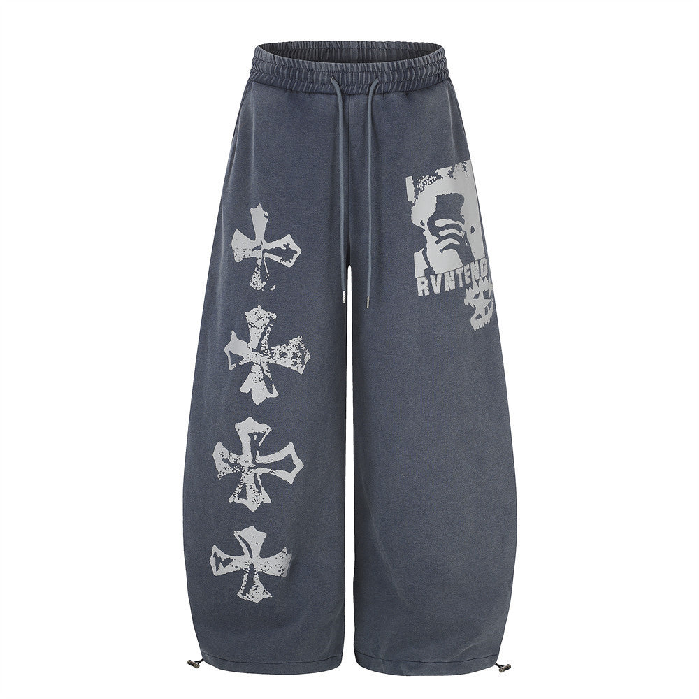 Wide-leg acid-wash sweatpants with distressed cross graphic print on left leg and character print on right thigh, shown in ch
