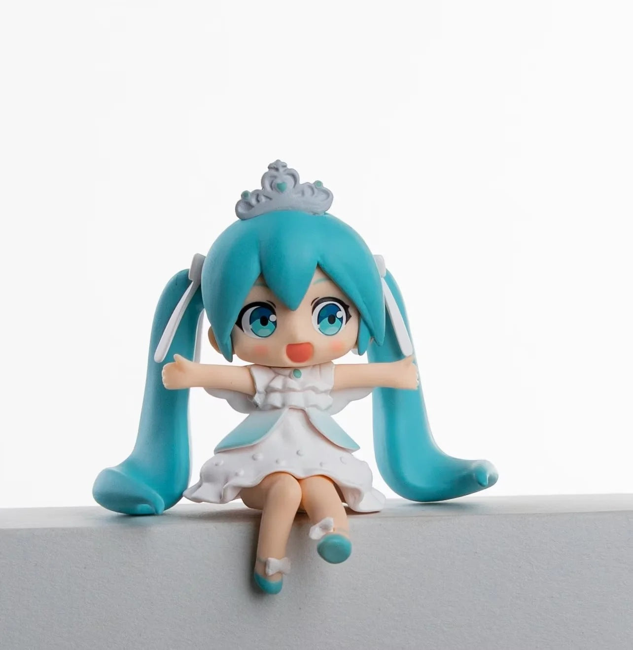 The Hatsune Miku Prayer Hugging Angel Princess 7.5cm PVC Figure Set features a small figurine with teal pigtails, a white dress, and crown. Its blue eyes, open arms, and excited expression captivate against a plain white backdrop.