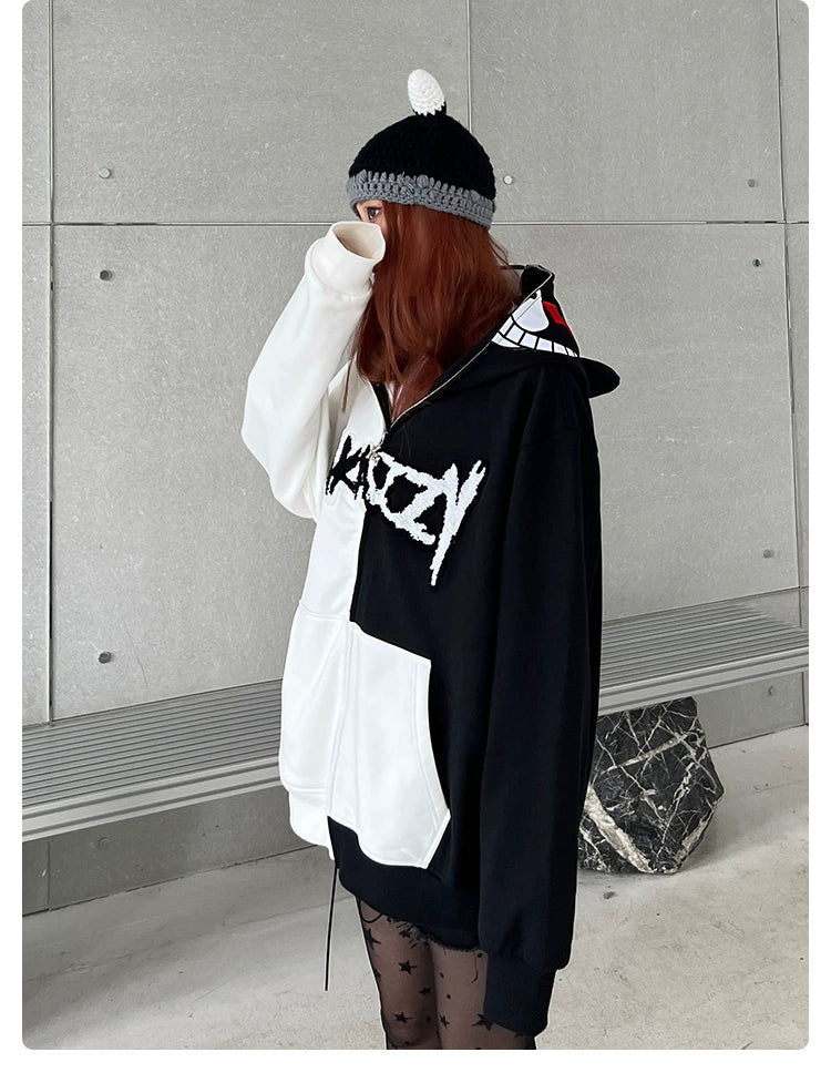 A person wears a Seakoff Monokuma-Inspired Hoodie, a 400GSM oversized black and white zip-up Danganronpa sweatshirt. They stand against a gray wall, donning a black-gray beanie with pom-pom and sheer star-patterned tights, with their face partly covered, perfect for Danganronpa fans.