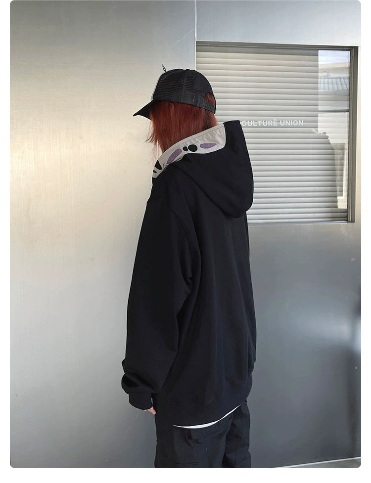 A person with long red hair and a black cap is wearing the Spirited Away No-Face Anime Hoodie, appealing to anime fans. They stand facing a metallic wall labeled &quot;CULTURE-UNION,&quot; capturing the essence of Spirited Away in their unique style.