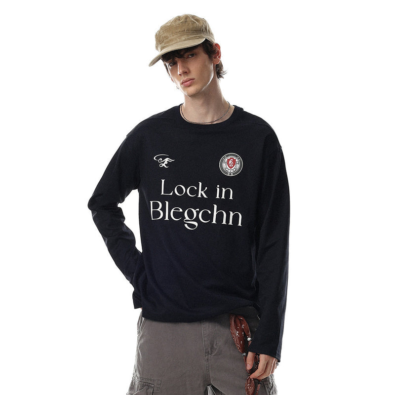 Black long sleeve crew neck tee worn by a model, front view with chest graphic and logo patch