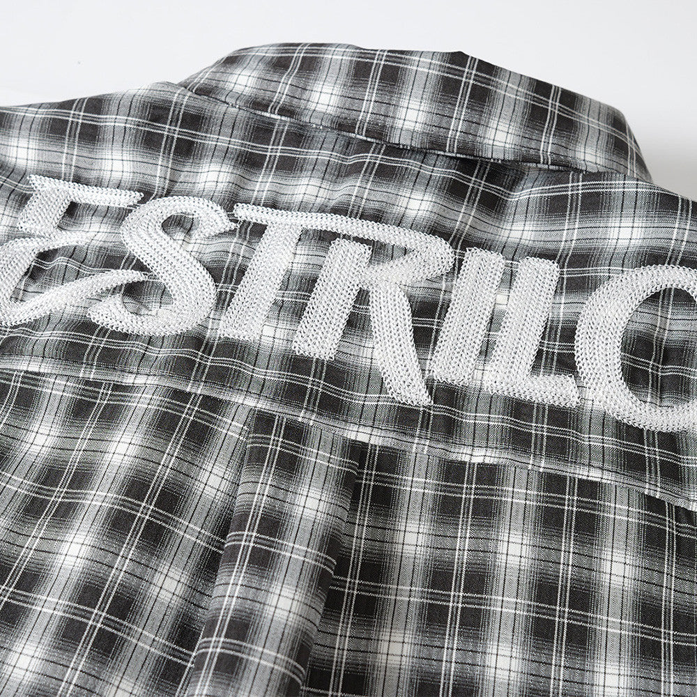 Close-up of white embroidered logo on black plaid shirt back yoke