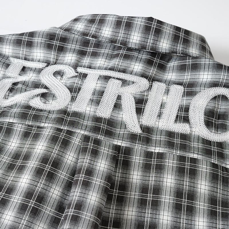 Close-up of white embroidered logo on black plaid shirt back yoke