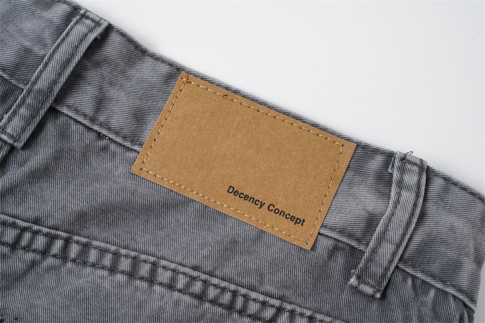 Tan waistband patch reading Decency Concept on washed grey jeans