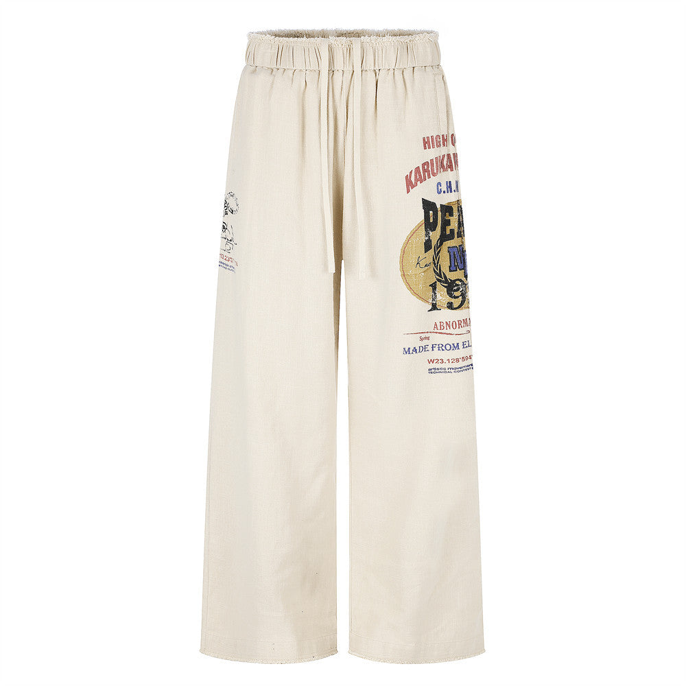 Wide-leg linen beige trousers with vintage graphic print on front leg, raw frayed waistband, and elastic drawstring waist