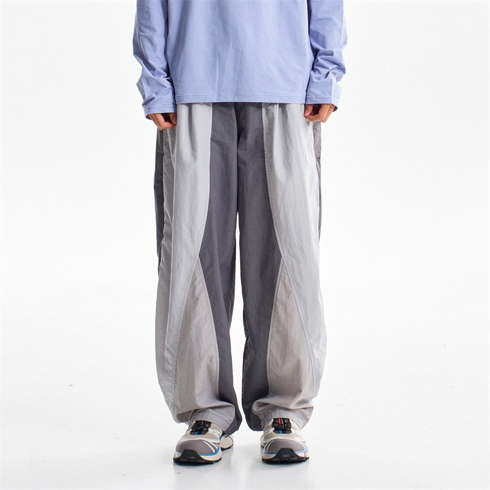Wide-leg two-tone colorblock track pants in grey with curved panel seams and elastic waistband, styled with trail sneakers