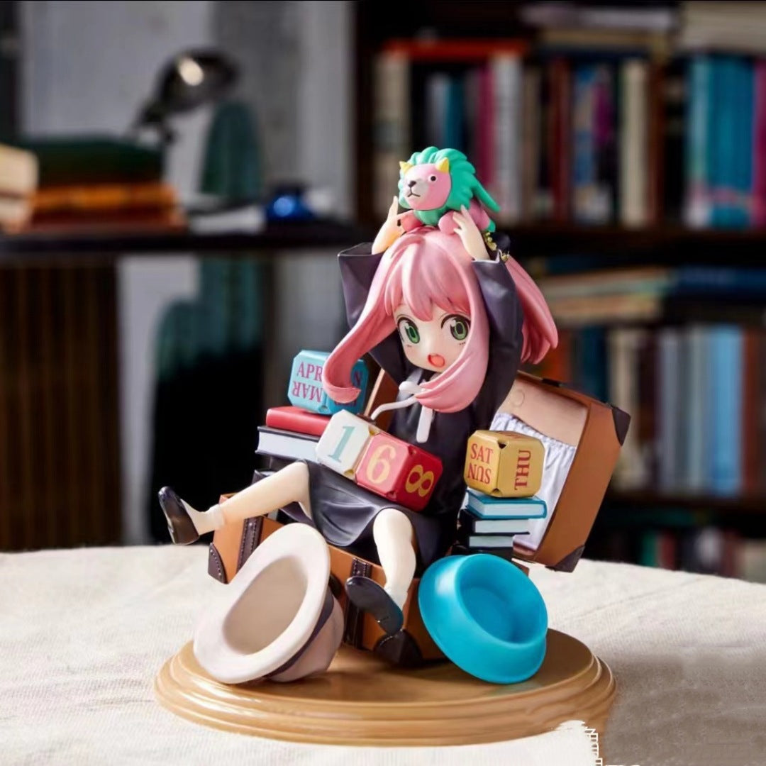 The Spy × Family Anya Forger PVC figure, inspired by the series, showcases a pink-haired girl in a black outfit with a green lion toy on her head, sitting among scattered books and blocks featuring numbers and &quot;SAT,&quot; surrounded by shelves.